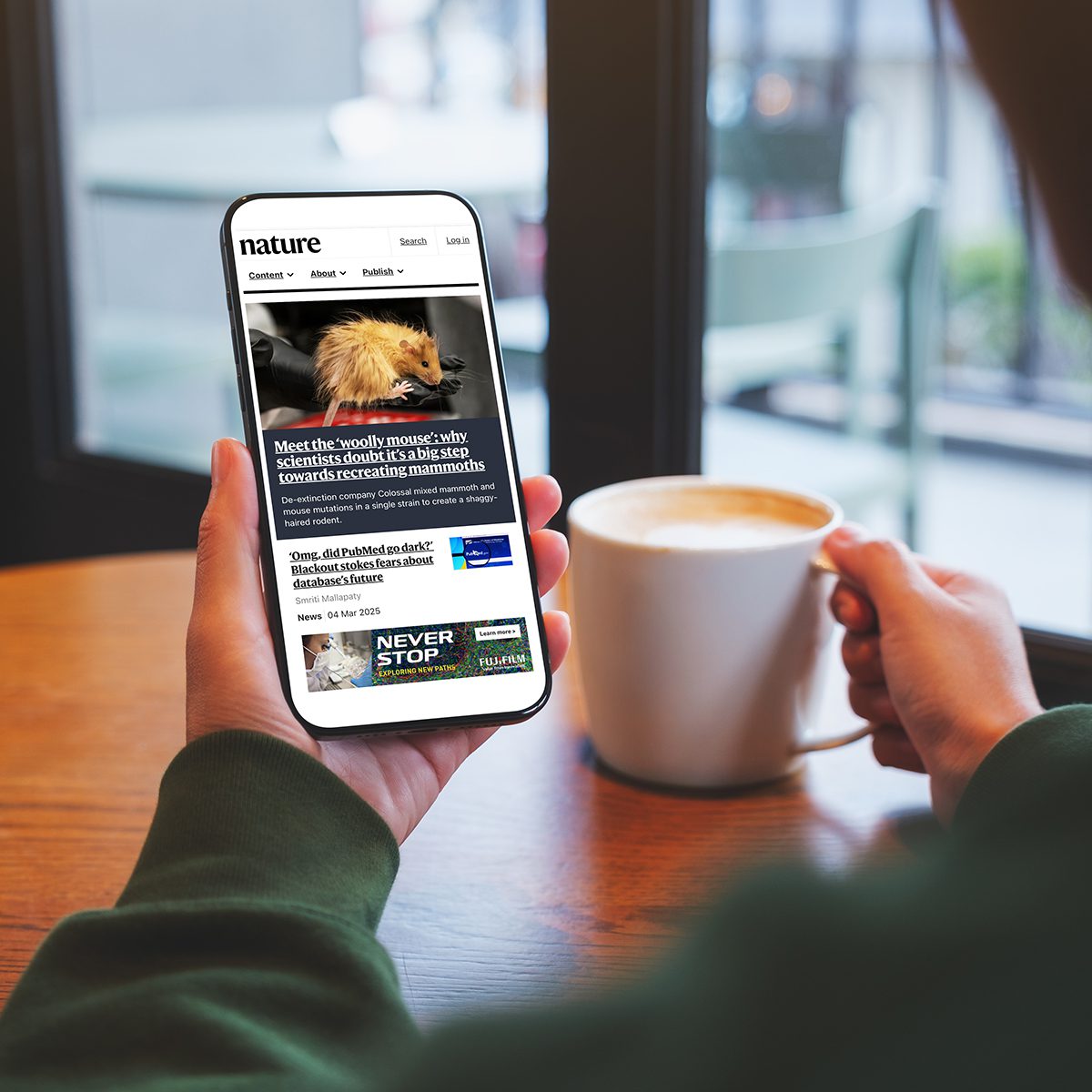 Mockup image of a woman holding mobile phone with nature.com on her screen while drinking coffee in cafe