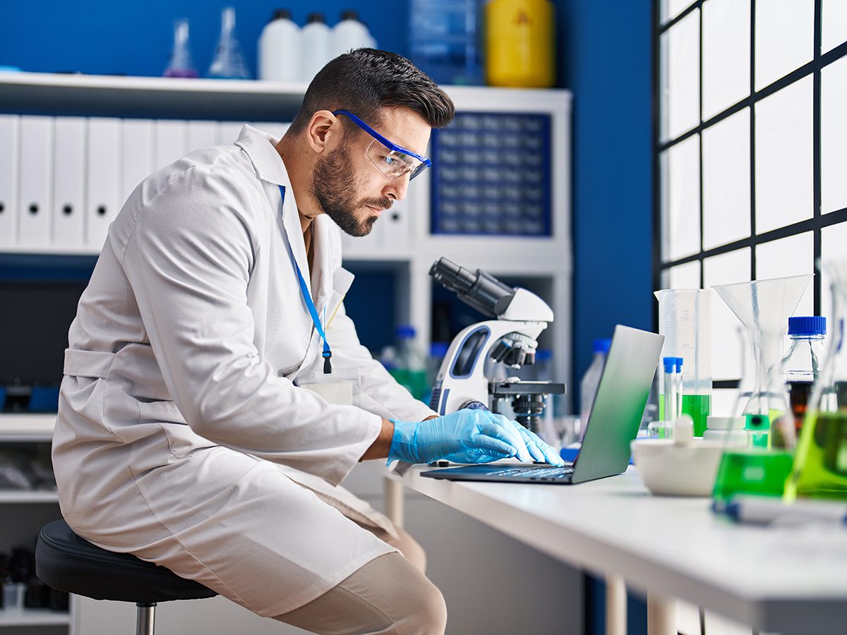 Male Hispanic clinical researcher using laptop and microscope at laboratory