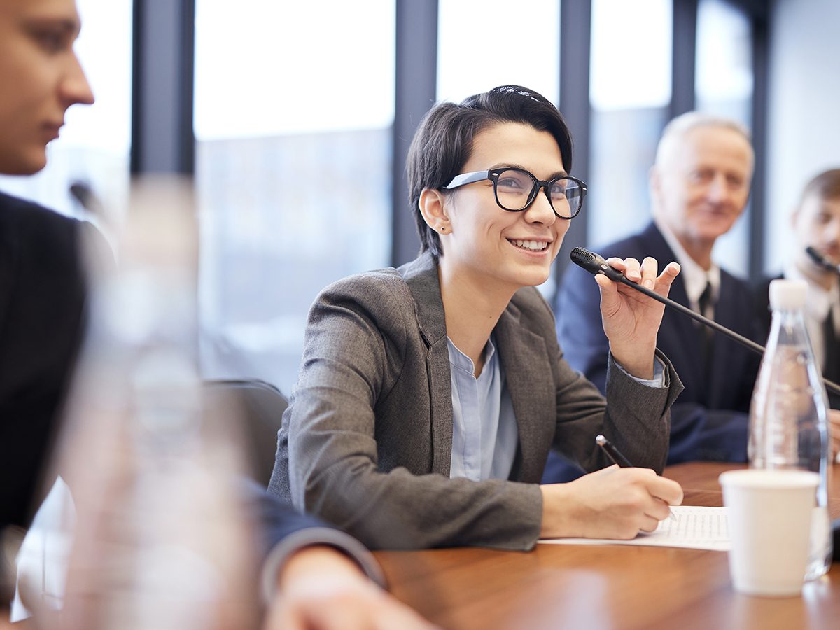 Portrait of smiling businesswoman speaking to microphone during conference or seminar