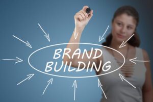 Brand Building - young businesswoman drawing information concept on transparent whiteboard in front of her