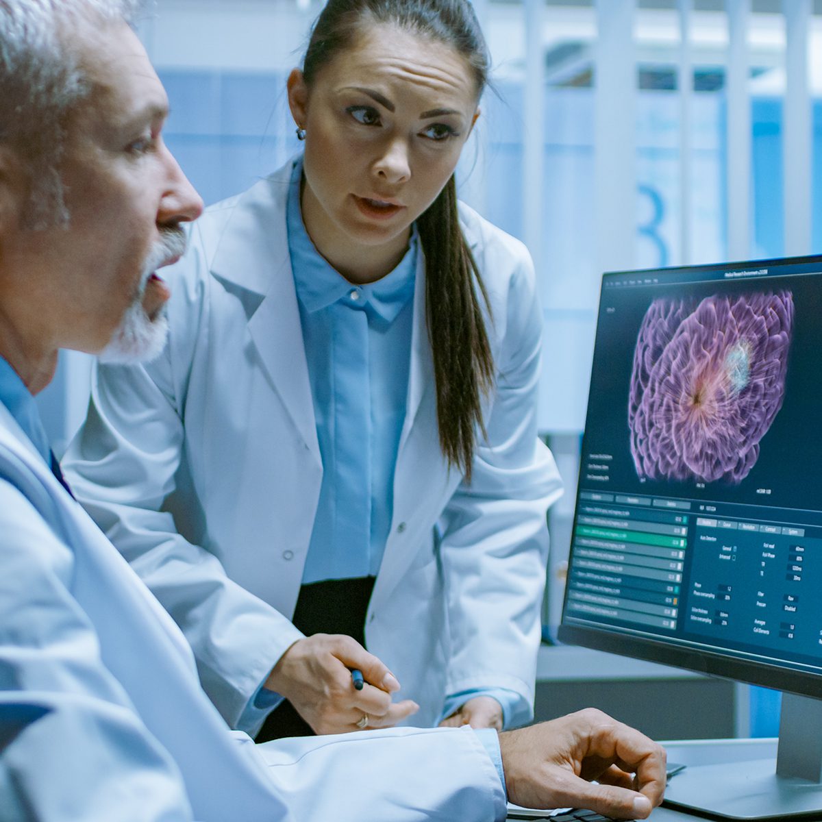 Two Medical Scientists in the Brain Research Laboratory Discussing Progress on the Neurophysiology Project Curing Tumors. Neuroscientists Use Personal Computer with MRI, CT Scans Show Brain Images.