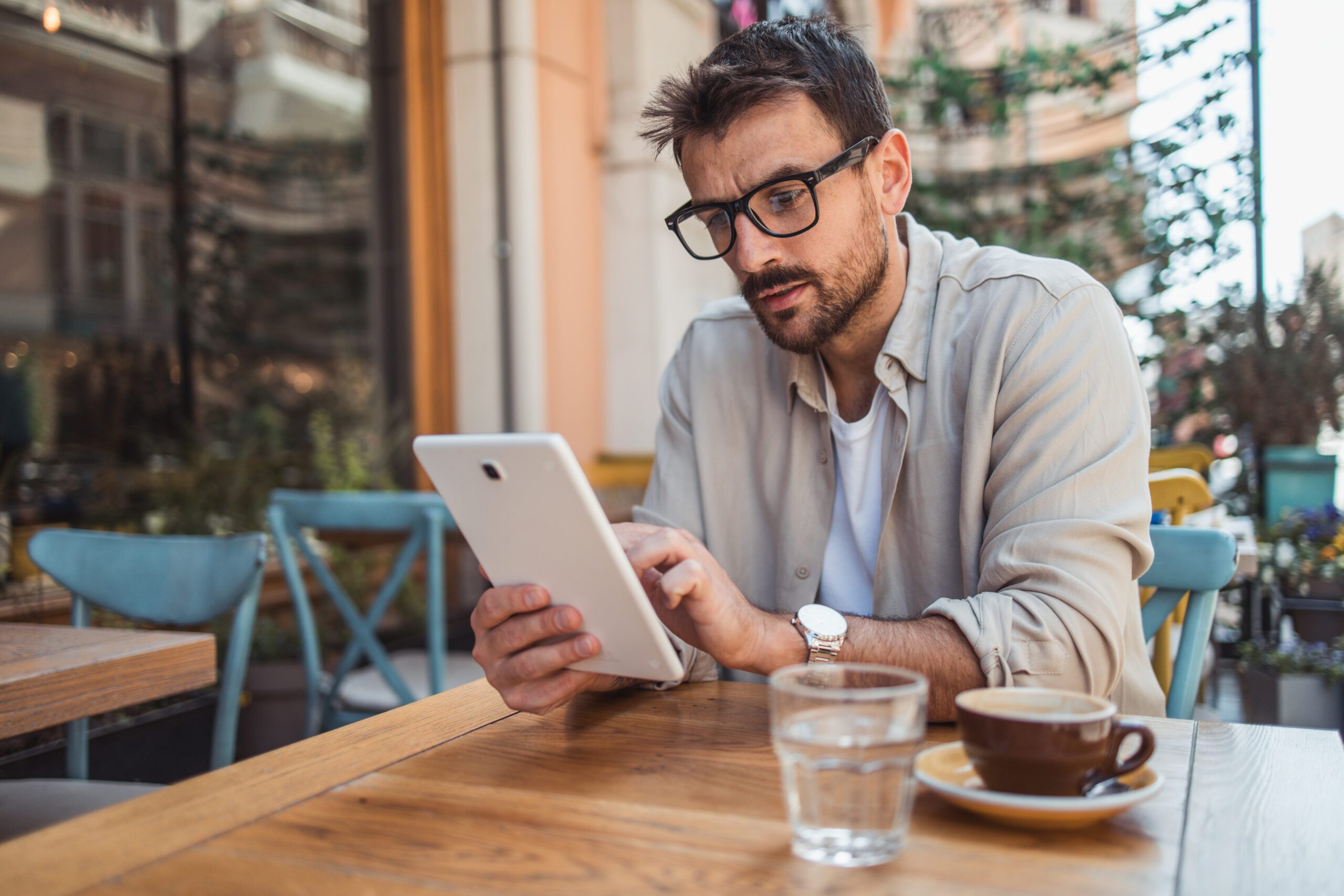 A man sits in the garden of a cafe on the promenade and uses a digital tablet