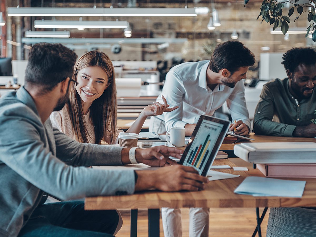 Group of young modern people in smart casual wear communicating and using modern technologies while working in the office